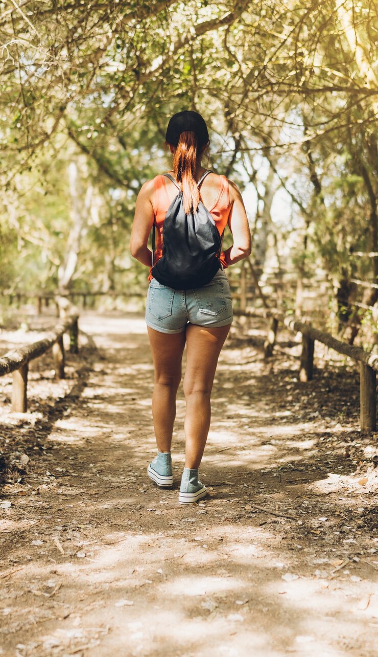 Foto vertical de la parte de atrás de una mujer caucásica de mediana edad caminando por un sendero rural con árboles a la sombra.