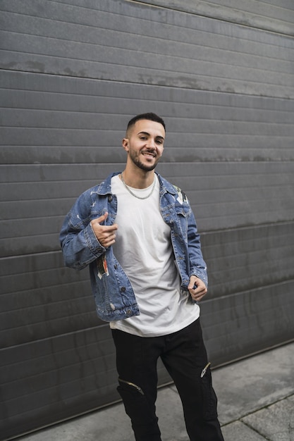 Foto vertical de un tipo elegante con un collar de cadena camiseta blanca chaqueta de jeans pantalones negros