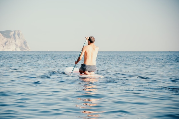 Foto vista lateral de um homem nadando e relaxando na prancha de sup Homem esportivo no mar na prancha de Stand Up Paddle SUP O conceito de uma vida ativa e saudável em harmonia com a natureza