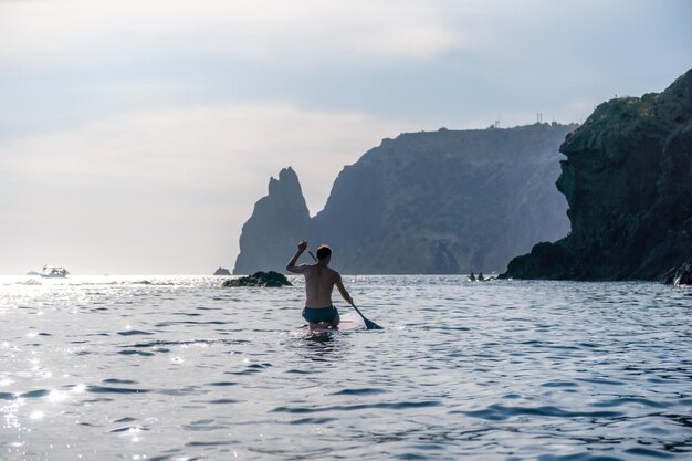 Foto vista lateral de um homem nadando e relaxando na prancha de sup Homem esportivo no mar na prancha de Stand Up Paddle SUP O conceito de uma vida ativa e saudável em harmonia com a natureza