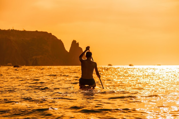 Foto de vista lateral de un hombre nadando y relajándose en el tablero sup hombre deportivo en el mar en el stand