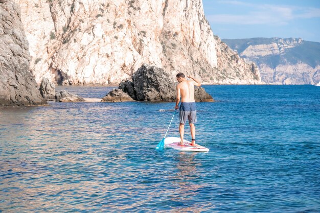 Foto de vista lateral de un hombre nadando y relajándose en el tablero sup hombre deportivo en el mar en el stand