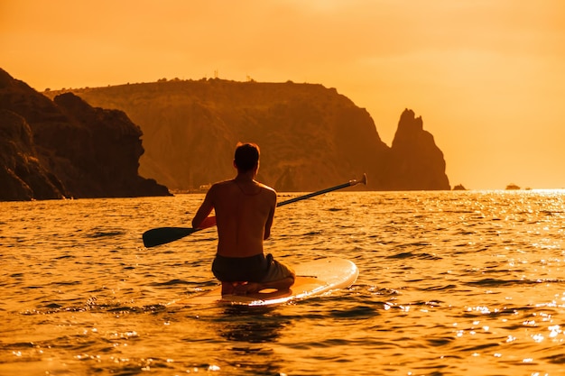 Foto de vista lateral de un hombre nadando y relajándose en el tablero sup hombre deportivo en el mar en el stand