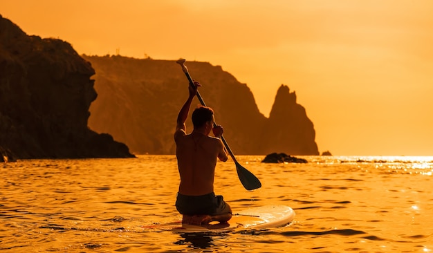 Foto de vista lateral de un hombre nadando y relajándose en el tablero sup hombre deportivo en el mar en el stand