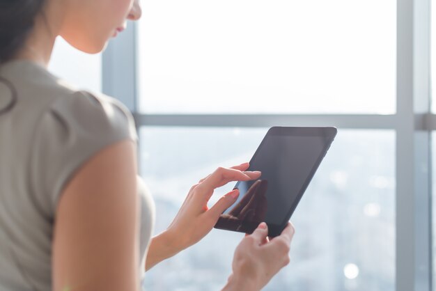 Foto de la vista lateral del joven teletrabajador femenino que usa la tableta, buscando y buscando información a través de la aplicación de conexión wi-fi en la oficina o en el hogar.