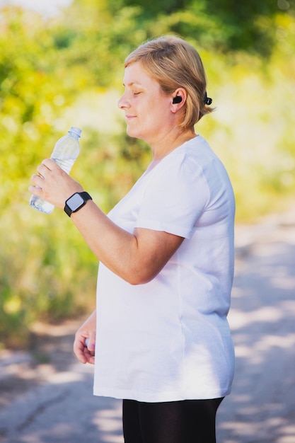 Foto de vista lateral de una mujer rubia al aire libre con ropa deportiva con reloj digital en la mano y ...