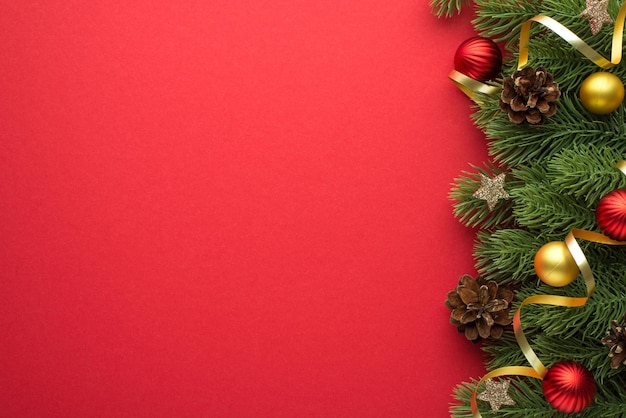 Foto de vista superior de bolas de árbol de navidad doradas y rojas piñas estrellas brillantes y serpentina dorada en ramas de pino sobre fondo rojo aislado con espacio vacío