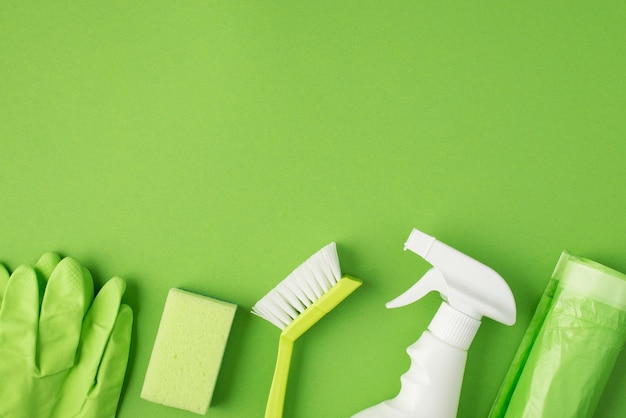 Foto de vista superior de bolsas de basura de esponja de cepillo de botella de spray de detergente blanco y guantes de goma verde sobre fondo verde aislado con espacio en blanco