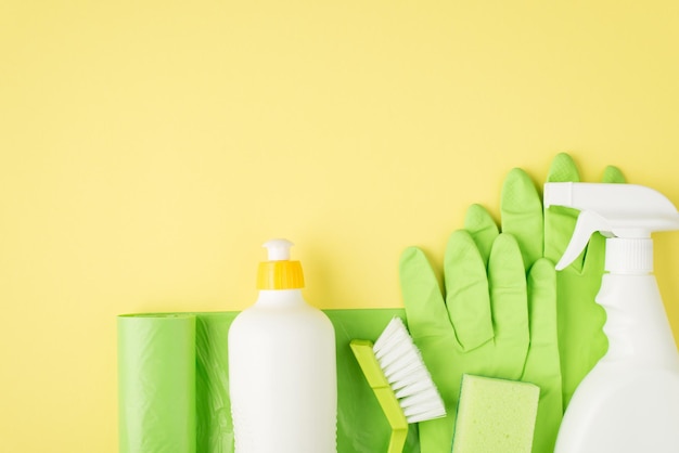 Foto de vista superior de bolsas de basura verdes, spray limpiador y botellas de gel, cepillo de esponja, guantes de goma sobre fondo amarillo aislado con espacio de copia