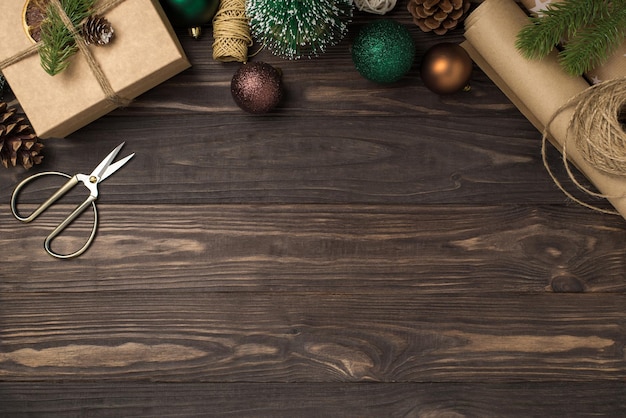 Foto de la vista superior de la caja de regalo, bolas de árbol de Navidad de oro verde, ramitas de pino, conos, herramientas de artesanía, tijeras, carretes de hilo y rollos de papel artesanal sobre fondo de escritorio de madera oscura aislado con espacio de copia