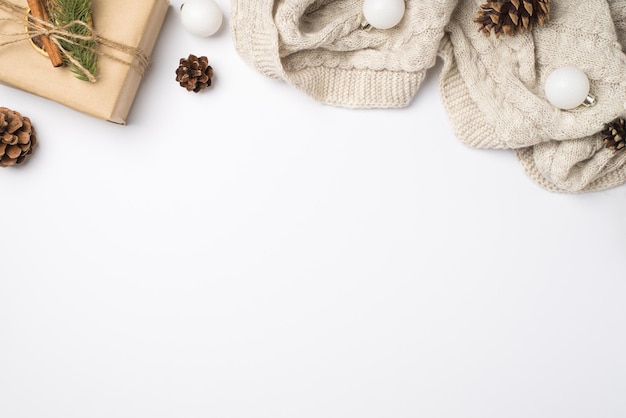 Foto de la vista superior de la caja de regalo de papel artesanal con lazo de cordel, ramita de pino, rodaja de limón seco, palito de canela, conos de suéter de punto acogedor y bolas de árbol de Navidad blancas sobre fondo blanco aislado con espacio vacío