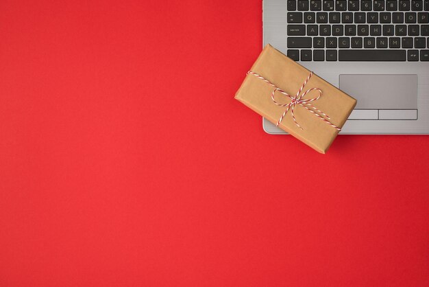 Foto de vista superior de caja de regalo de papel artesanal rectangular con lazo de hilo en una computadora portátil gris sobre fondo rojo aislado con espacio de copia