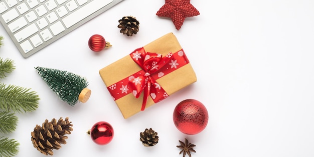 Foto de vista superior de caja de regalo con teclado de lazo rojo bolas de árbol de navidad rojo conos de ramitas de juguete de pino estrella y anís sobre fondo blanco aislado con espacio en blanco