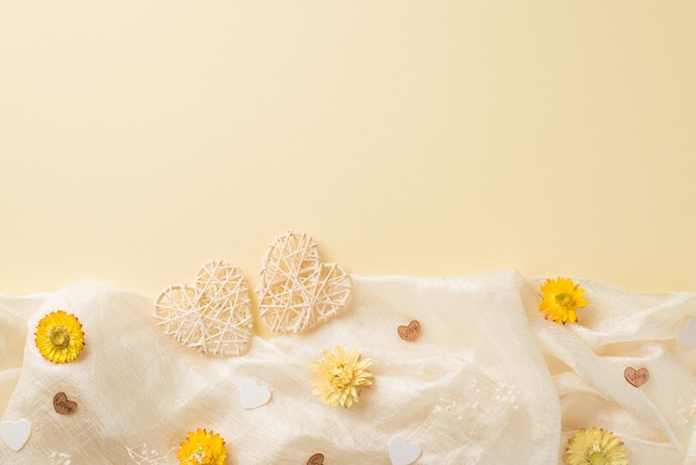 Foto de la vista superior de la composición del día de la mujer flores de campo amarillas y blancas y dos corazones de ratán sobre textil blanco suave sobre fondo beige aislado con espacio de copia