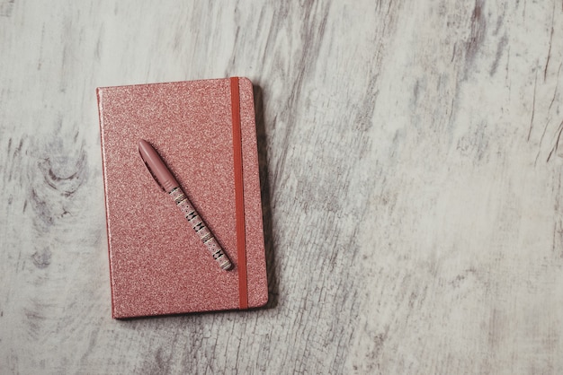 Foto de vista superior de un cuaderno cerrado con tapa brillante y un bolígrafo en la superficie de madera gris