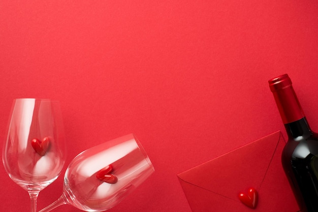 Foto de la vista superior de las decoraciones del día de san valentín corazones pequeños en dos copas de vino sobre rojo cerrado y botella de vino sobre fondo rojo aislado con espacio de copia