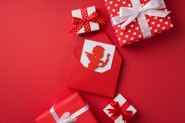 Foto de la vista superior de las decoraciones del día de san valentín sobre rojo abierto con tarjeta y silueta de cupido cajas de regalo rojas y blancas sobre fondo rojo aislado con copyspace