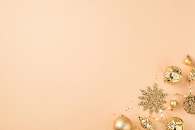 Foto de vista superior de decoraciones doradas para árboles de navidad conos de copos de nieve bolas serpentinas y confeti sobre fondo beige aislado con espacio vacío