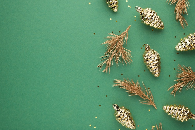 Foto de la vista superior de decoraciones navideñas conos de juguetes dorados ramitas de pino dorado y confeti sobre fondo verde aislado con espacio vacío