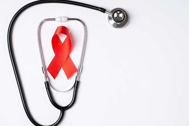 Foto de la vista superior del estetoscopio y el símbolo de la cinta de seda roja de la concienciación sobre el sida en un fondo blanco aislado con espacio en blanco