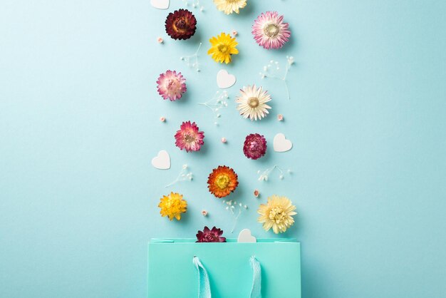Foto de vista superior de la explosión de composición del día de la mujer de flores silvestres y corazones de una bolsa de regalo azul sobre fondo azul pastel aislado