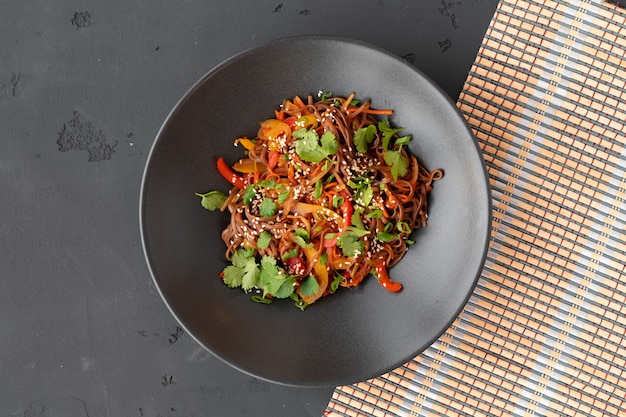 Foto de la vista superior de fideos wok con verduras y carne en un tazón sobre fondo gris