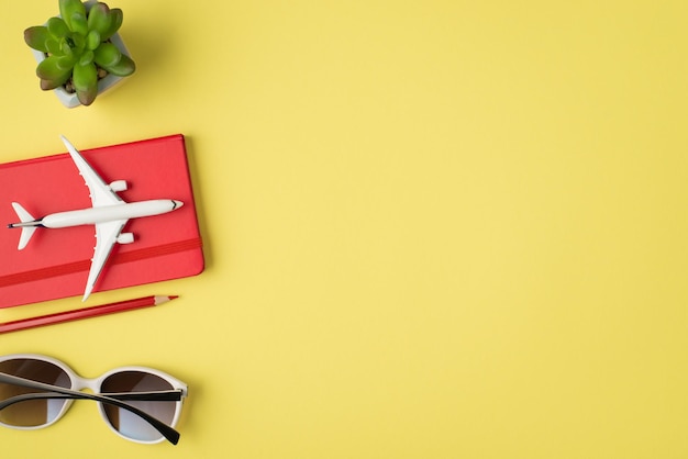Foto de vista superior de la foto de vista superior de gafas de sol de maceta y modelo de avión en cuaderno rojo sobre fondo amarillo pastel aislado con espacio de copia