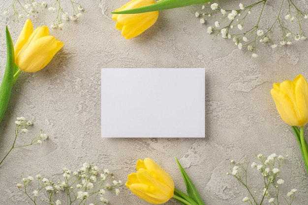 Foto de la vista superior de la hoja de papel de composición del día de la mujer tulipanes amarillos y gypsophila blanca sobre fondo de hormigón gris texturizado aislado con espacio de copia