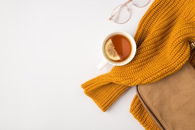 Foto de la vista superior de un jersey amarillo, bolso de cuero beige, gafas elegantes y una taza de té con limón sobre fondo blanco aislado con espacio de copia