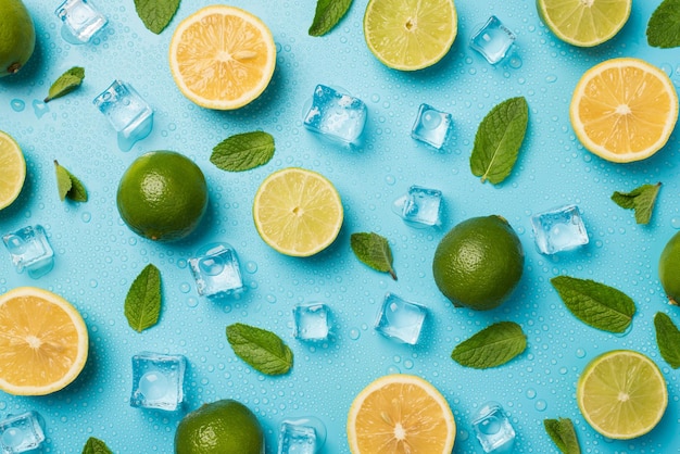 Foto de vista superior de limas cortadas y enteras en rodajas limones hojas de menta cubitos de hielo y gotas de agua sobre fondo azul pastel aislado