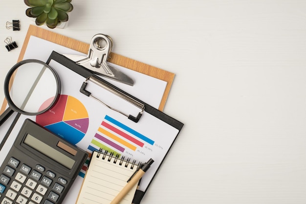Foto de la vista superior del lugar de trabajo de negocios con dos carpetas, diagrama de gráfico circular, carpetas de plantas, lupa, calculadora, cuaderno y bolígrafo sobre fondo blanco aislado con espacio de copia