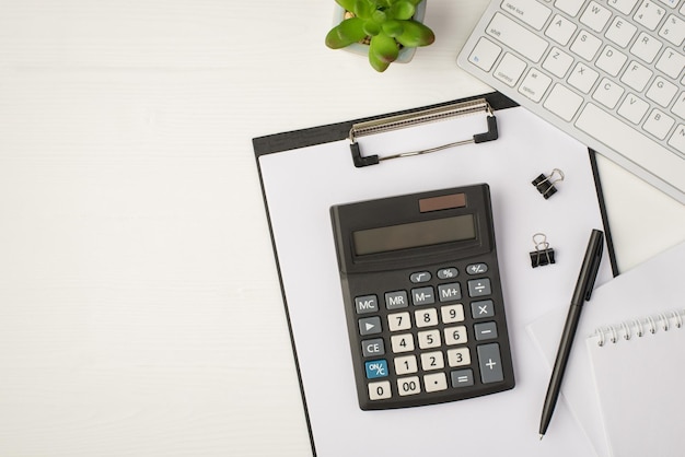 Foto de vista superior del lugar de trabajo de negocios con teclado macetero pluma carpetas papeles de cuaderno y calculadora en carpeta sobre fondo blanco aislado con copyspace