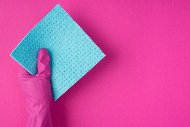 Foto de vista superior de la mano en guante rosa sosteniendo una servilleta azul sobre fondo rosa aislado con espacio de copia