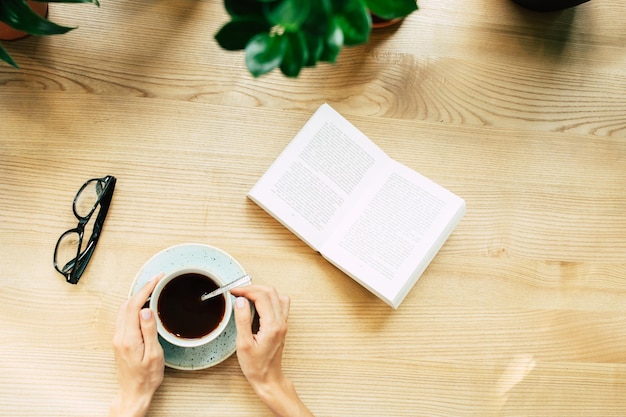 Foto de vista superior de manos femeninas con taza de café en la mesa de madera y vasos y libro