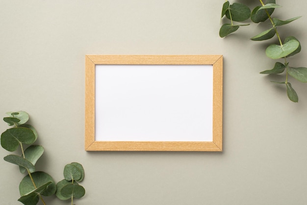 Foto de vista superior de marco de fotos de madera y ramas de eucalipto sobre fondo gris pastel con espacio vacío