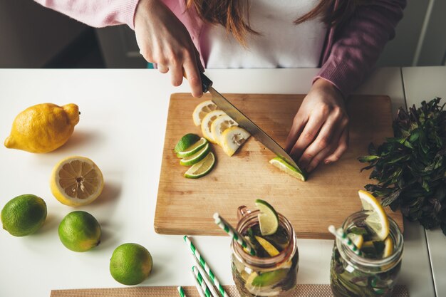 Foto de la vista superior de una mujer cortando frutas y haciendo un mojito de limón y lima