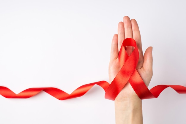 Foto de la vista superior en primera persona de la mano femenina sosteniendo una cinta roja rizada en la palma símbolo de concienciación sobre el sida en un fondo blanco aislado con espacio vacío