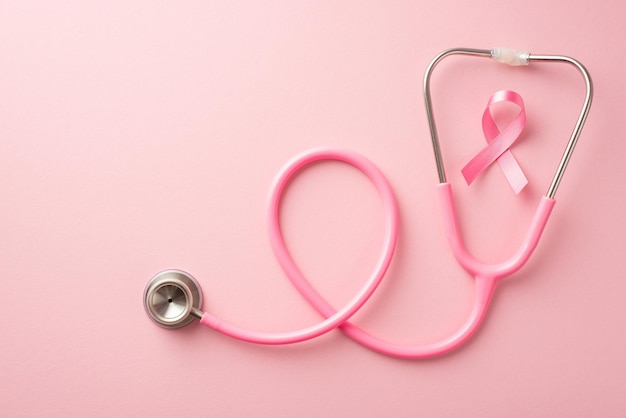 Foto de vista superior del símbolo de la cinta de seda rosa de la conciencia del cáncer de mama y estetoscopio sobre fondo rosa pastel aislado