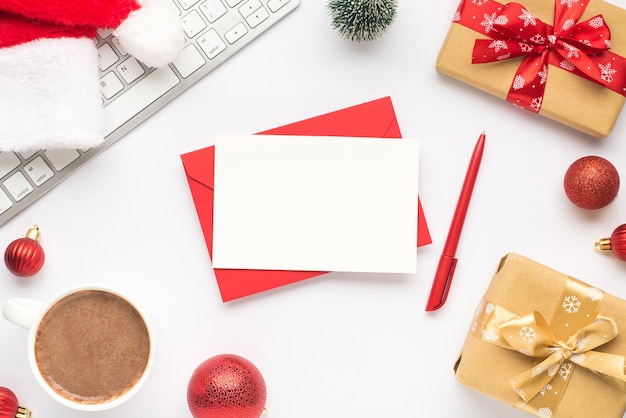 Foto de la vista superior de la taza del teclado de bebida caliente santa claus sombrero pino juguete rojo árbol de navidad bolas cajas de regalo con lazos de cinta hoja de sobre rojo y pluma sobre fondo blanco aislado con espacio vacío