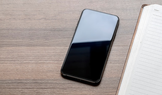 Foto de vista superior del teléfono inteligente con pantalla en blanco y cuaderno sobre la mesa.