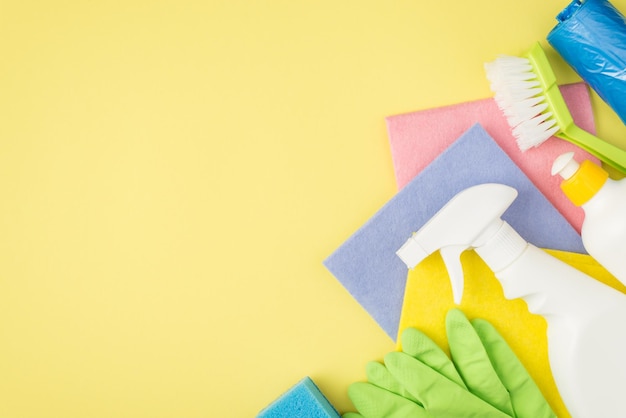 Foto de vista superior de trapos multicolores guantes de goma cepillar bolsas de basura de esponja azul spray y botellas de detergente en gel sobre fondo amarillo aislado con espacio de copia