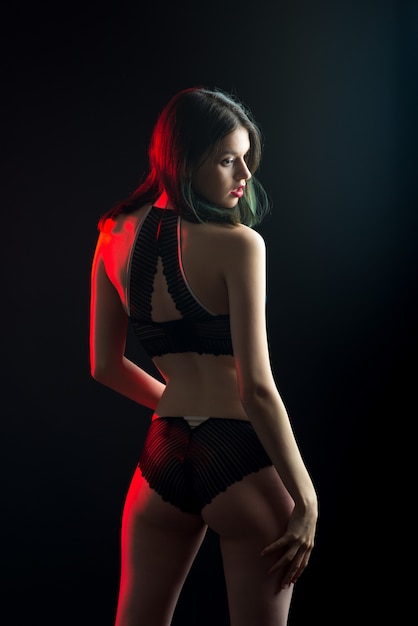 Foto de vista vertical hermosa dama tímida en bragas de sujetador de boudoir de bikini de encaje. Tierna delgada forma delgada pared negra aislada