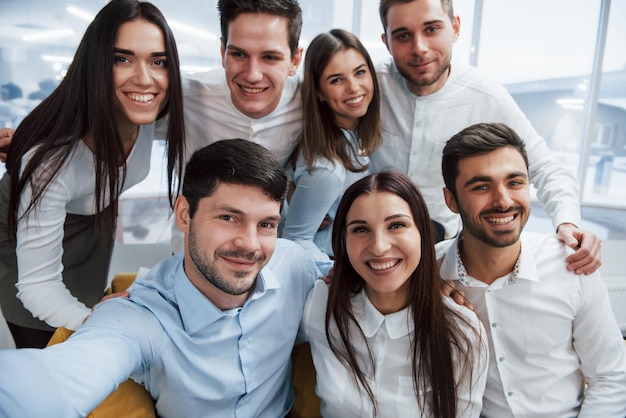 Foto vom Telefon Junges Team macht ein Selfie in klassischer Kleidung im modernen gut beleuchteten Büro