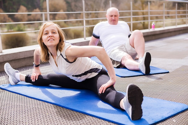 Foto von älterem Ehepaar, das sich im Freien auf Gymnastikteppichen streckt