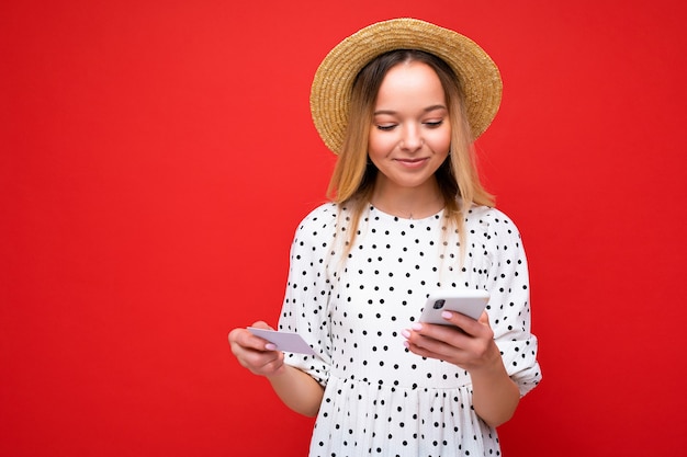 Foto von attraktiver positiver blonder Frau in Sommerkleidung, die Handy benutzt und Kreditkarte hält