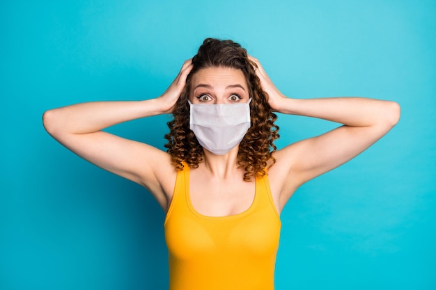 Foto von aufgeregten Studentenmädchenhänden Kopf erstaunt Blick Kamera tragen Maske gelbes Unterhemd isoliert blauer Farbhintergrund