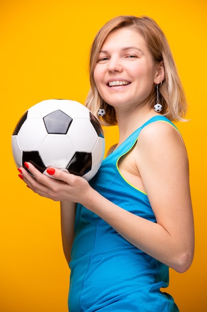 Foto von Blondine mit Fußball auf gelbem Hintergrund im Studio