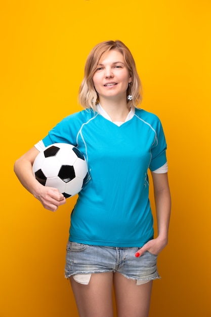 Foto von Blondine mit Fußball auf gelbem Hintergrund im Studio