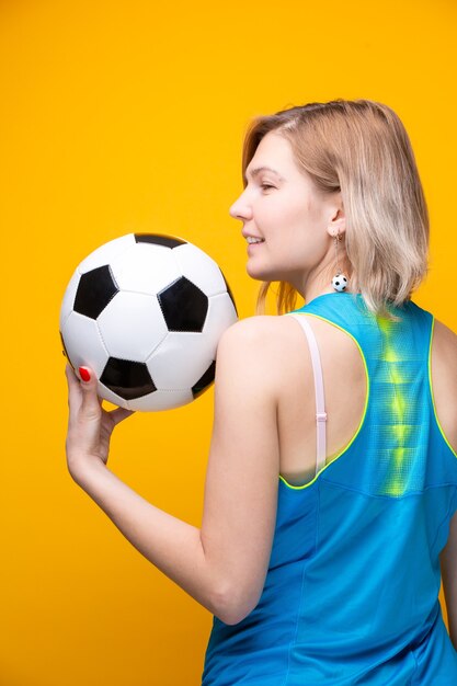 Foto von der Rückseite einer Blondine mit Fußball auf gelbem Hintergrund im Studio