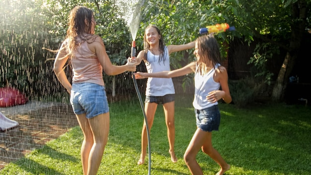 Foto von drei fröhlichen Mädchen im Teenageralter, die im Hinterhofgarten-Udner-Gartenwasserschlauch tanzen dancing